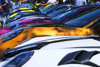 A lineup of colorful cars parked side by side at an outdoor car meet.