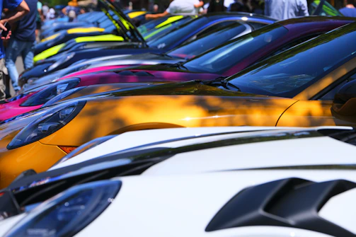 A lineup of colorful cars parked side by side at an outdoor car meet.