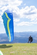 Close-up of a pilot preparing a paraglider wing on a grassy hill with panoramic mountain views.