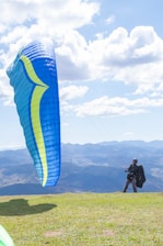 A student preparing their paraglider on a sunny hillside with mountains in the background.
