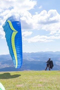 Close-up of a pilot preparing a paraglider wing on a grassy hill with panoramic mountain views.