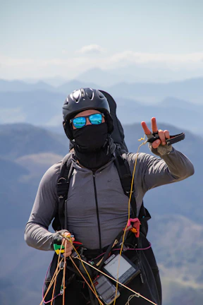 Close-up of a smiling pilot preparing a paraglider harness against mountain scenery.