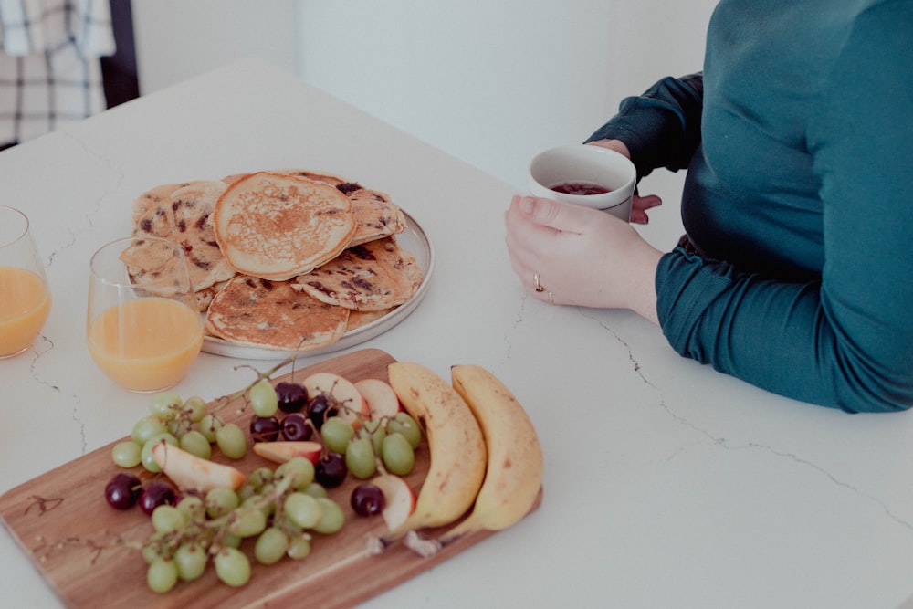 a woman sitting at a table with a plate of fruit and pancakes