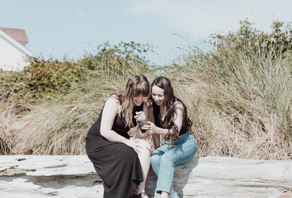 two girls sitting on a rock looking at a cell phone
