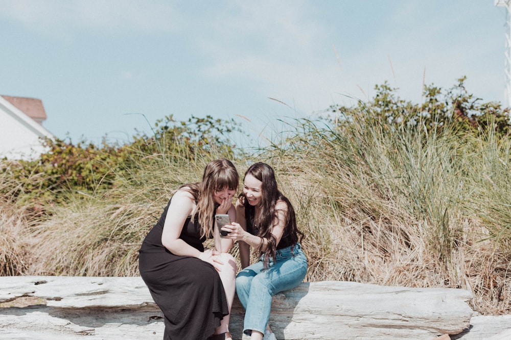 two girls sitting on a rock looking at a cell phone