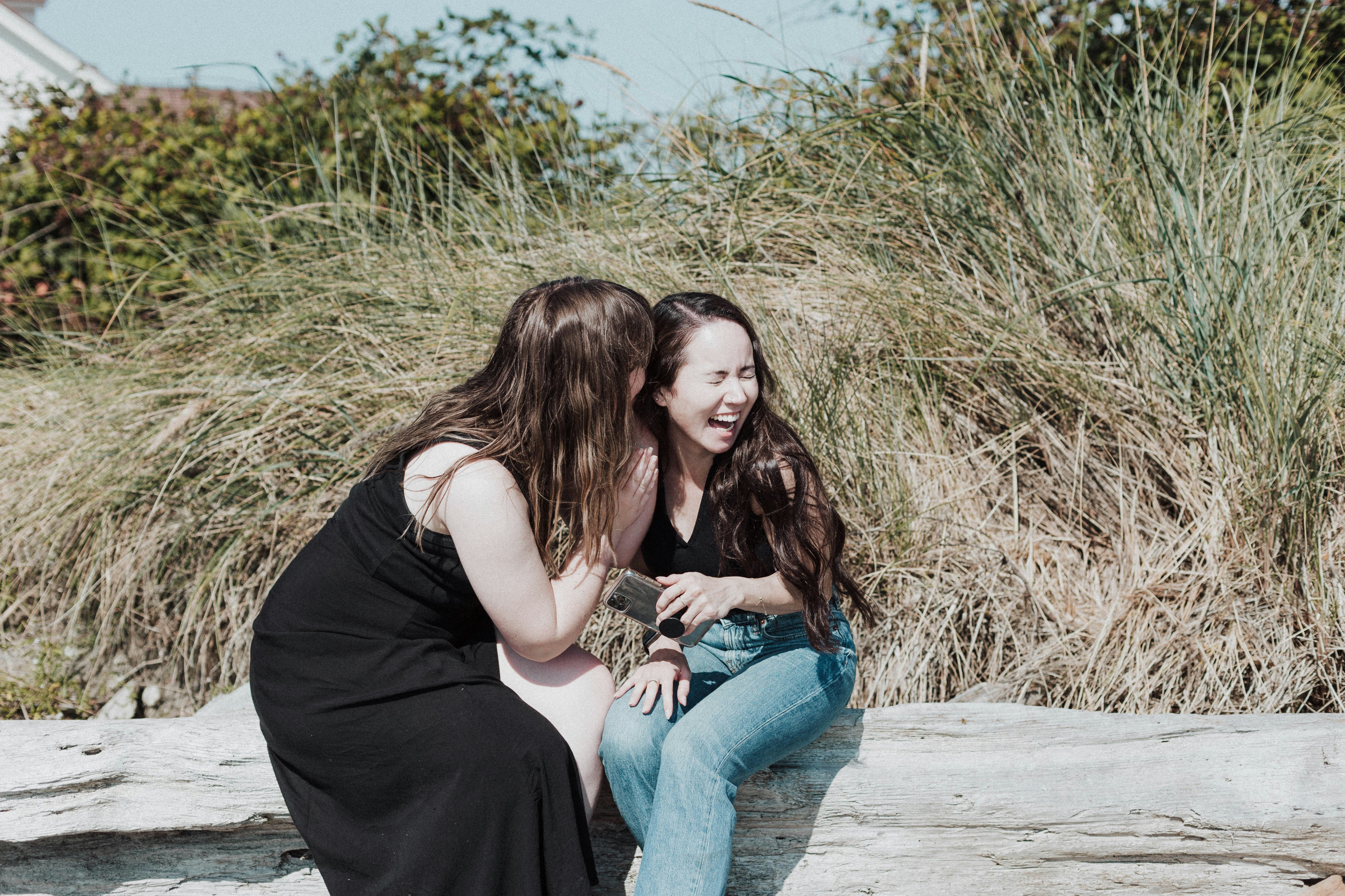 Two women sitting on a log talking