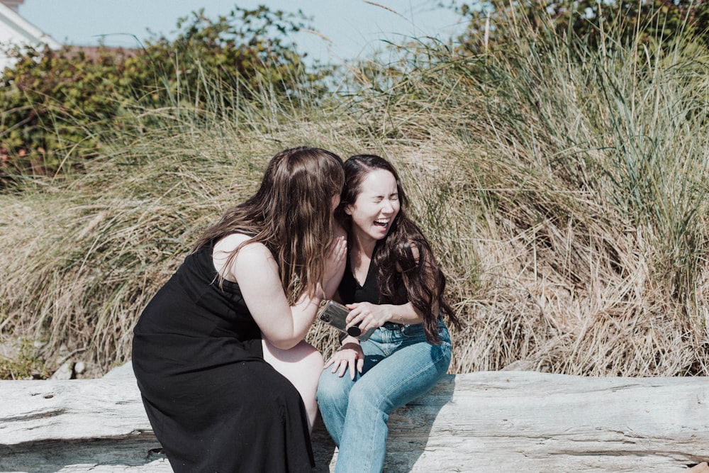 two women sitting on a log talking to each other