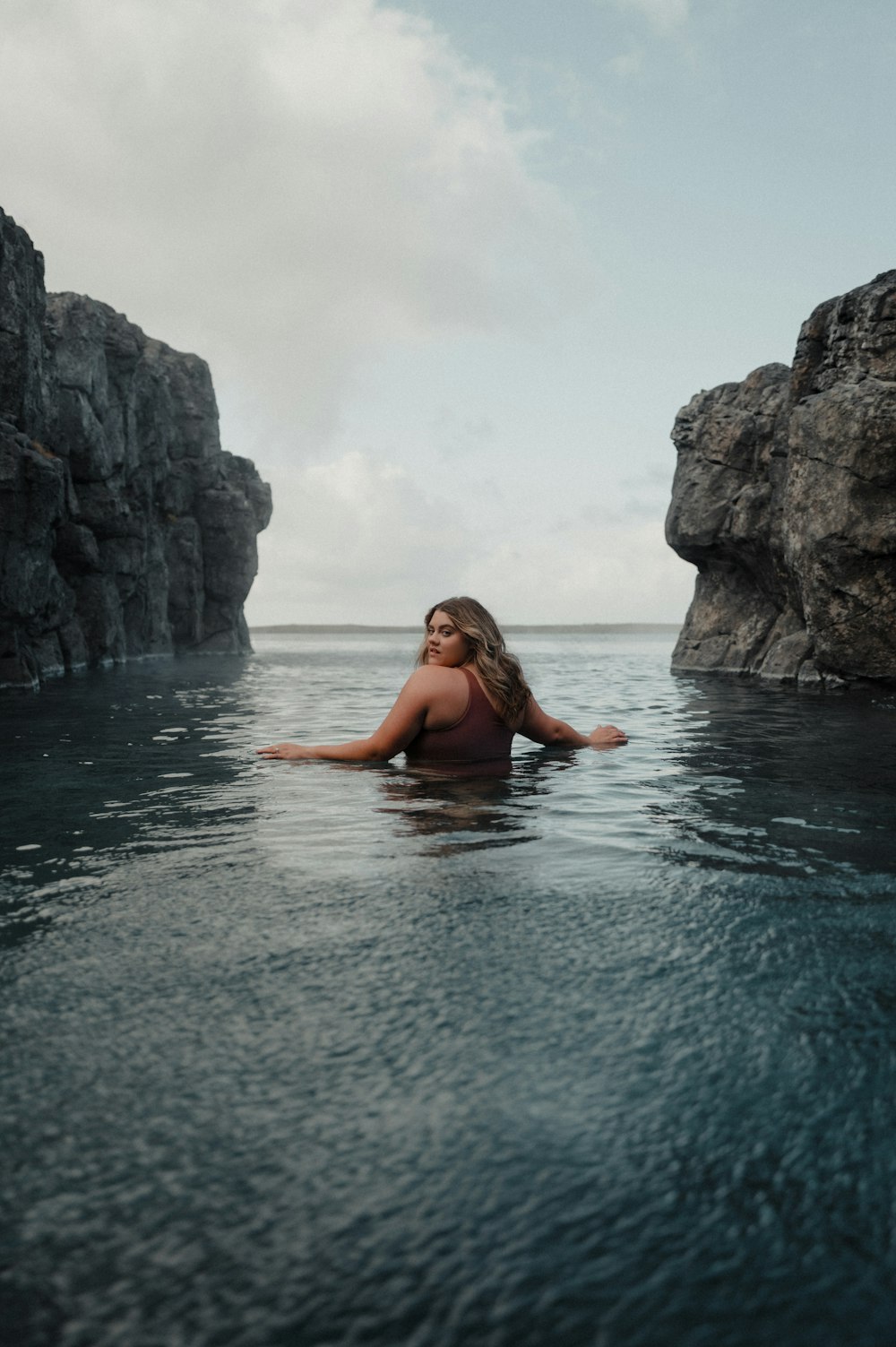 a woman in a body of water with rocks in the background