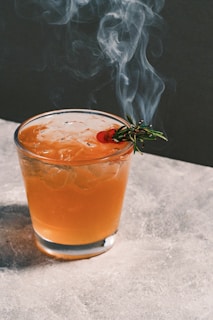 A vibrant cocktail being poured into a glass with smoke rising.
