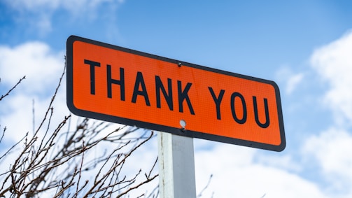 A hopeful veteran smiling warmly while holding a 'Thank You' sign outdoors.