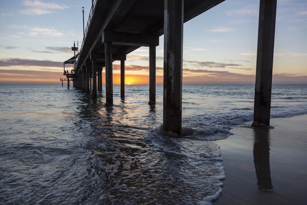 a view of the ocean under a pier at sunset