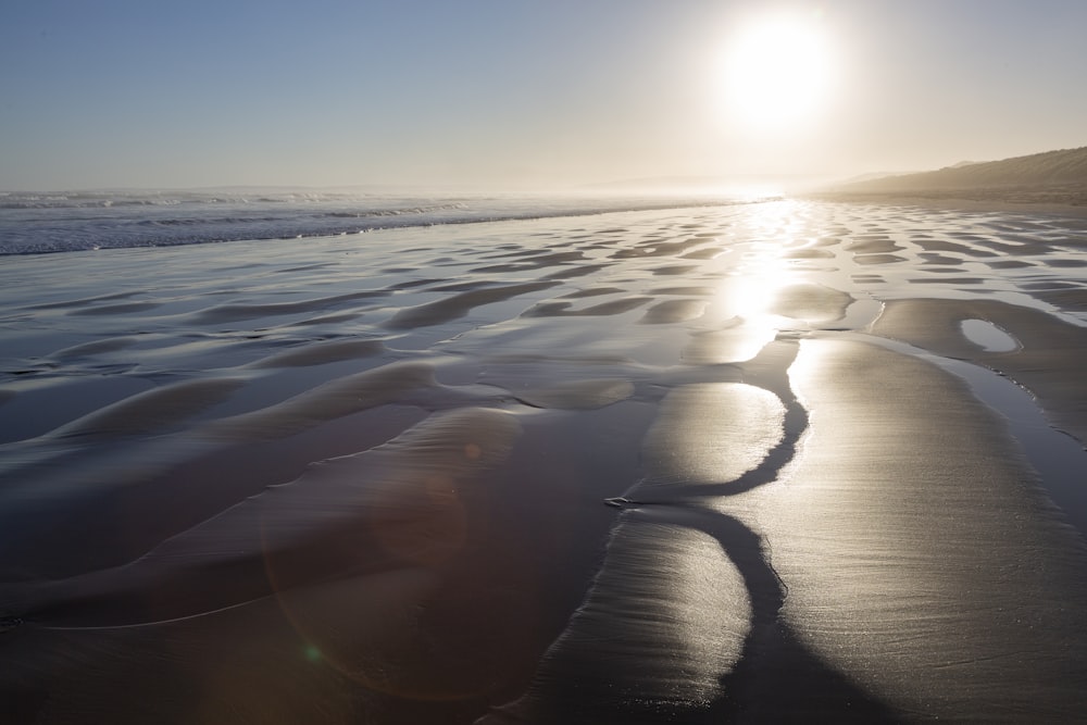 the sun is shining over the water on the beach