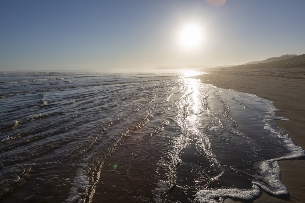 the sun is shining over the water on the beach