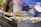 A food stall displaying trays of assorted grilled skewers and rolls. A person is seen holding skewers and tending to the food. The background shows a blue tarp and some yellow decorations.
