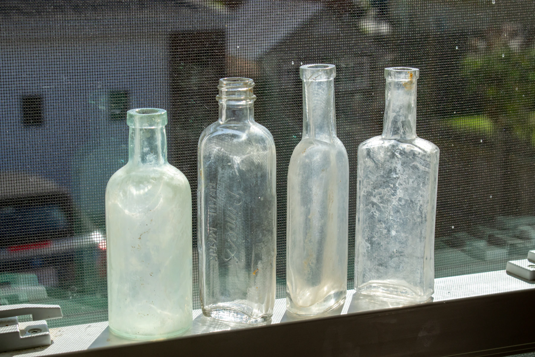 Four old clear glass bottles of different shapes standing in a row on a window sill