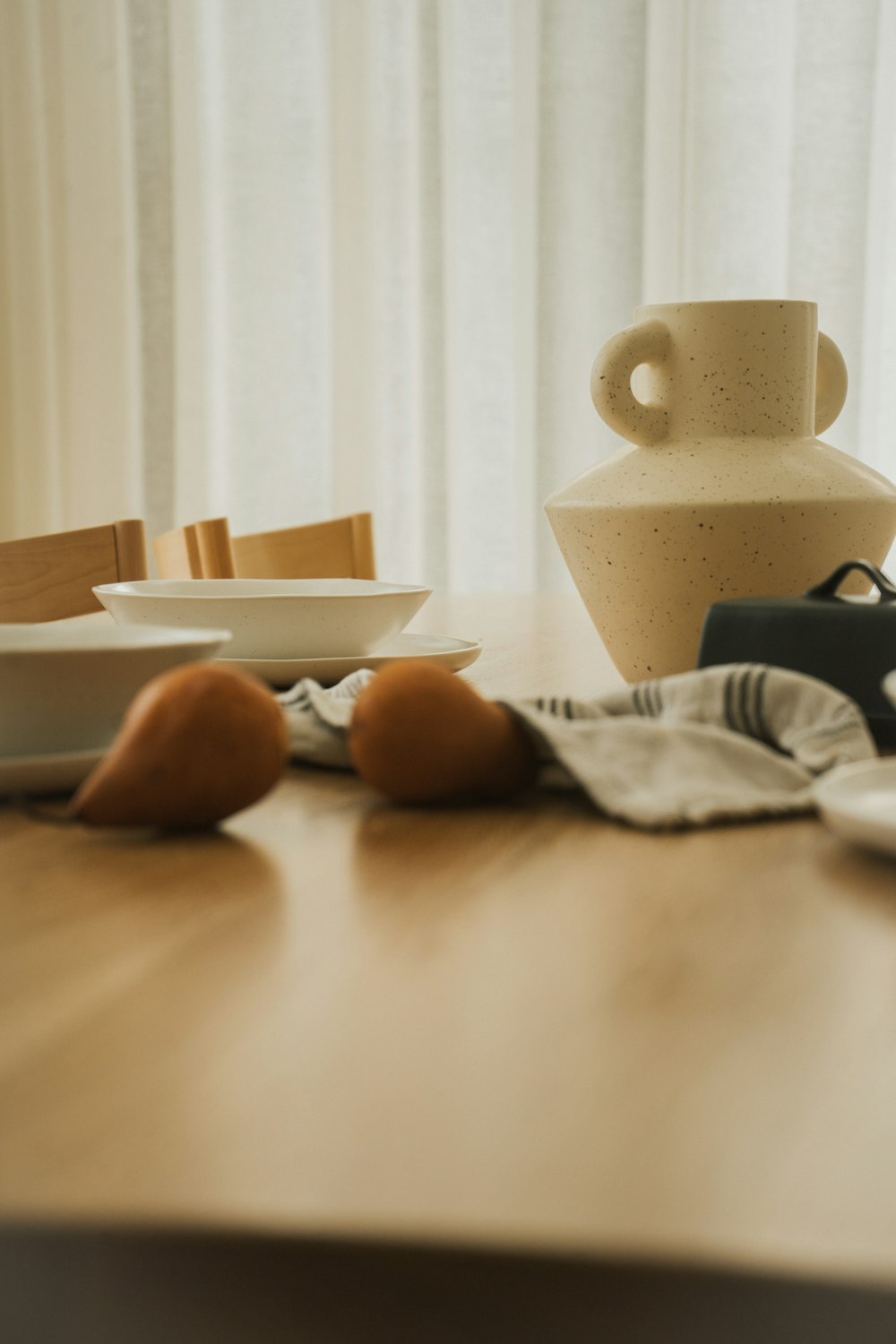 a wooden table topped with a white vase and plates