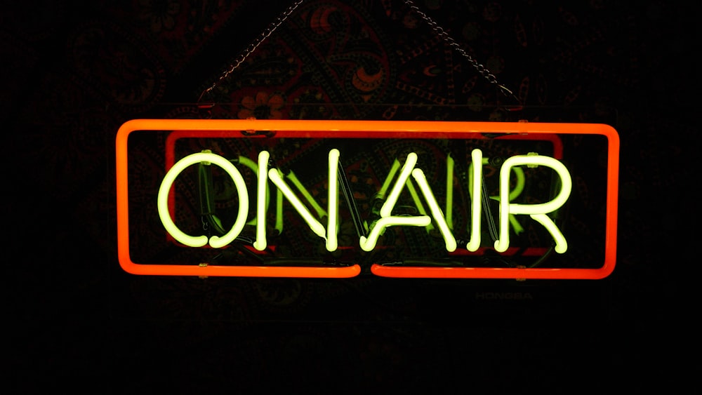 a neon sign that says on air hanging from a chain