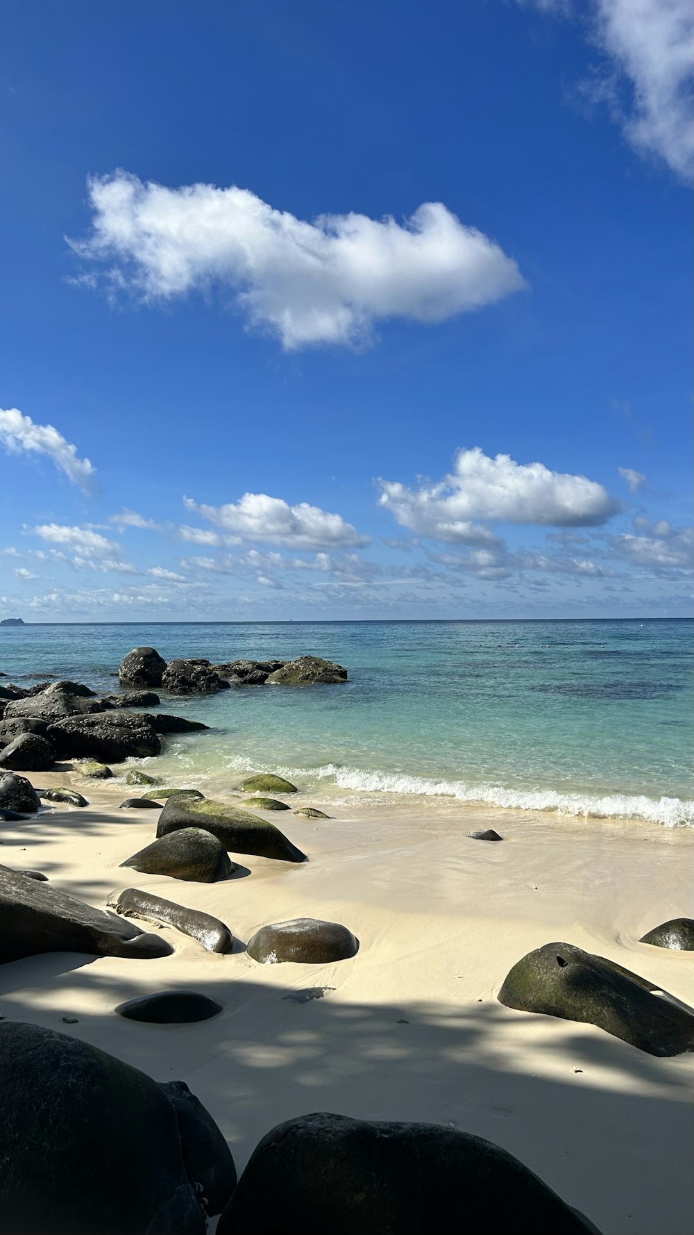 a beach with rocks and water under a cloudy blue sky