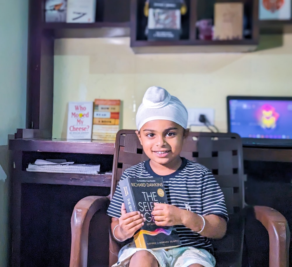 a young boy sitting in a chair holding a book