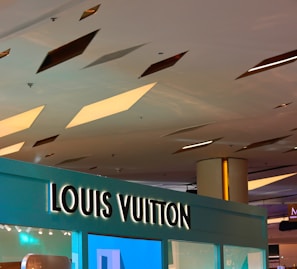 A ceiling with geometric cutouts and recessed lighting above a store with a prominent Louis Vuitton sign. The store display is modern with a sleek design.
