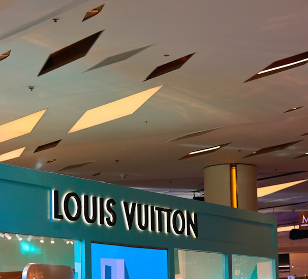 A ceiling with geometric cutouts and recessed lighting above a store with a prominent Louis Vuitton sign. The store display is modern with a sleek design.