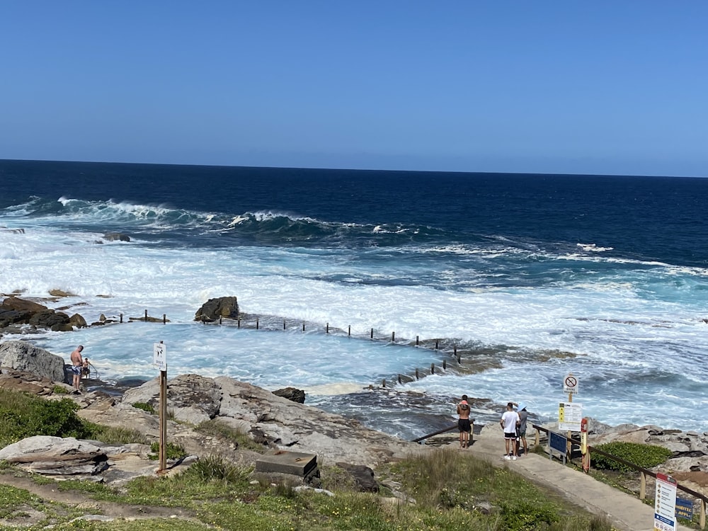 a group of people standing on top of a cliff near the ocean