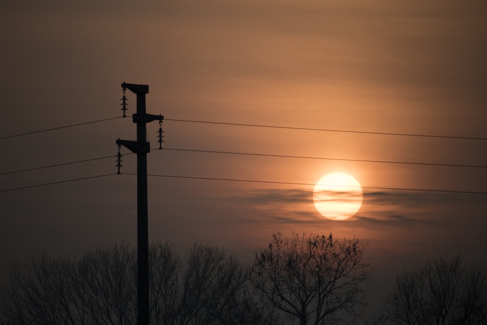 the sun is setting behind a telephone pole