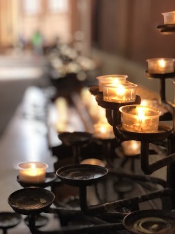 Close-up of vibrant votive candles glowing warmly on a wooden shelf.