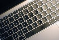 A close-up view of a laptop keyboard with black keys and white letters. The keyboard features shortcut icons and a matte finish.