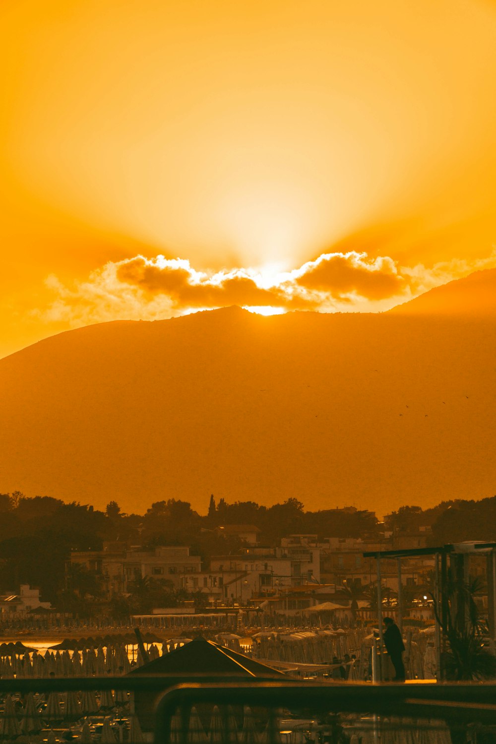 the sun is setting over a city with a mountain in the background