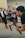 A photographer is holding a professional camera mounted on a stabilizer, capturing a scene with a blurred crowd in the background. A person in motion, dressed in traditional clothing, appears in the background, adding a dynamic element to the composition.