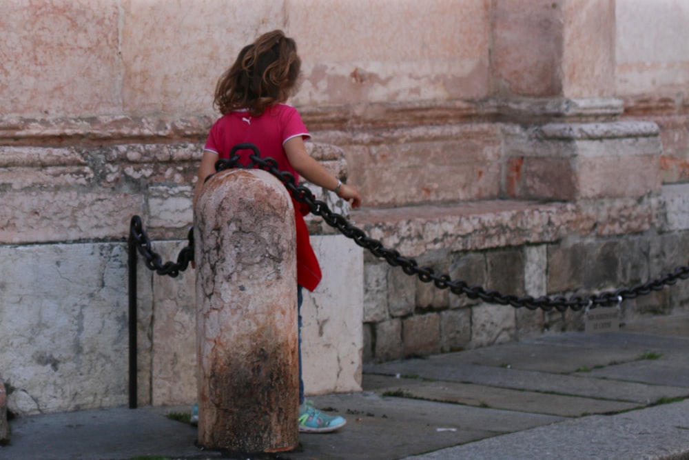 a little girl in a red shirt is holding a chain