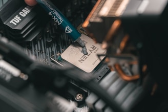 A close-up view of a computer's motherboard with a Ryzen processor installed. A thermal compound is being applied to the processor using a syringe labeled MX-4, indicating a step in assembling or upgrading computer hardware.