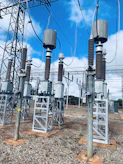High-voltage electrical substation under clear blue sky with workers inspecting equipment.