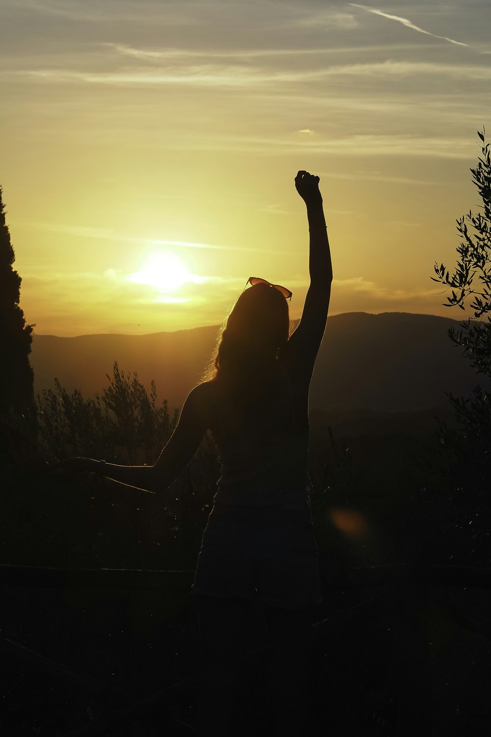 a woman raising her arms in the air at sunset
