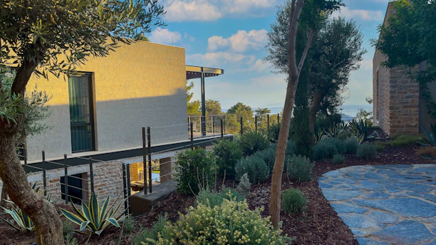 Elegant townhouse with minimalist architecture surrounded by a manicured garden and golden light.