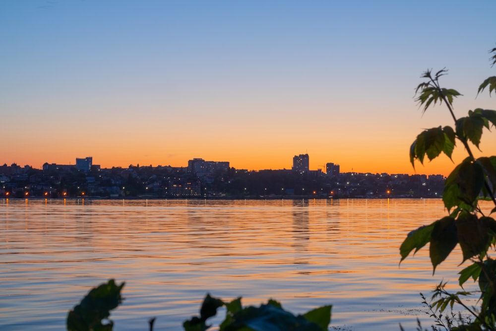 the sun is setting over the water with a city in the background