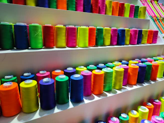 Colorful spools of 3D printing filament neatly arranged on a shelf.