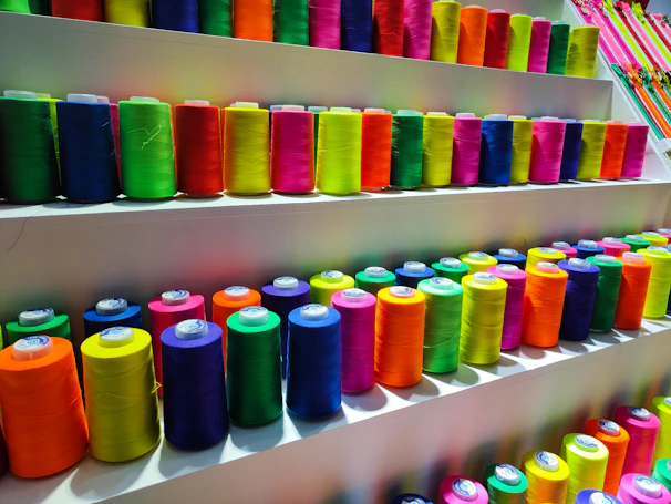 Colorful spools of 3D printing filament neatly arranged on a shelf.
