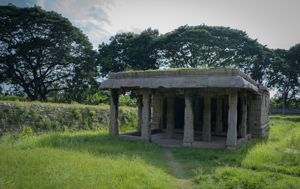 a stone structure in a grassy field with trees in the background