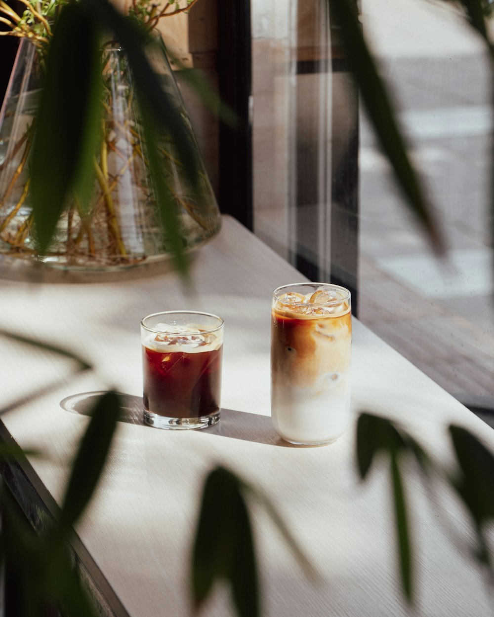 two drinks sitting on a table next to a vase of flowers