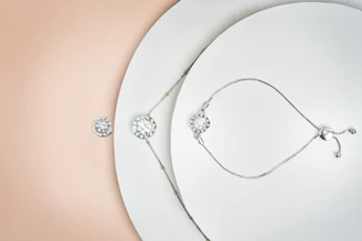 A close-up of minimalistic silver jewelry displayed on a soft fabric background.