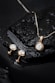 Elegant jewelry pieces, including a gold pendant with a large diamond and matching earrings, displayed on a wet, glossy black stone surface with water droplets.