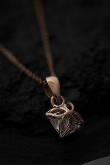 A close-up view of a gold pendant with an intricate floral design hanging from a delicate chain. The pendant rests on a dark textured surface, creating a contrast that highlights the shine and details of the jewelry.