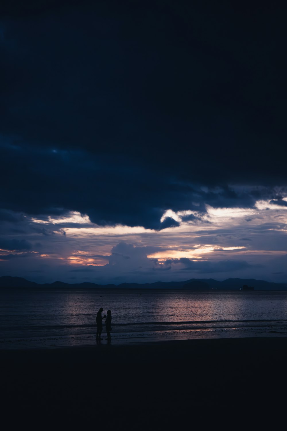 two people standing on a beach under a cloudy sky