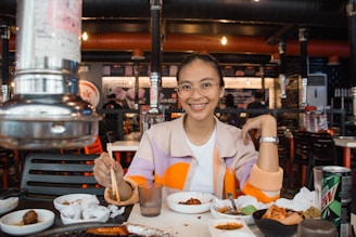 A cheerful young woman enjoying her meal at a cozy, modern Japanese street-food style restaurant.
