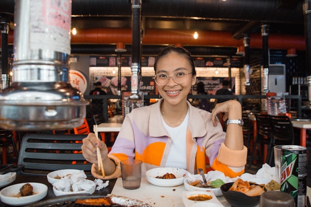 A cheerful young woman enjoying her meal at a cozy, modern Japanese street-food style restaurant.