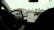 View from inside a car showing a driver with hands on the steering wheel, focusing on the dashboard and an integrated touchscreen displaying navigation information. The car appears to be stopped at an intersection, with visible traffic lights ahead.