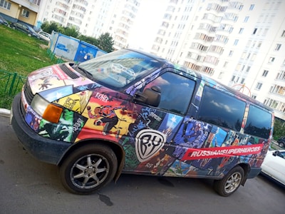 A van covered with vibrant comic-style art depicting various superheroes. The illustrations feature dynamic poses and bold colors. The hashtag '#RUSSIANSUPERHEROES' is prominently displayed on the side.