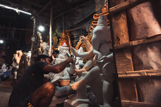 Artisan carefully painting a vibrant Ganesh idol in a warm, festive workshop.
